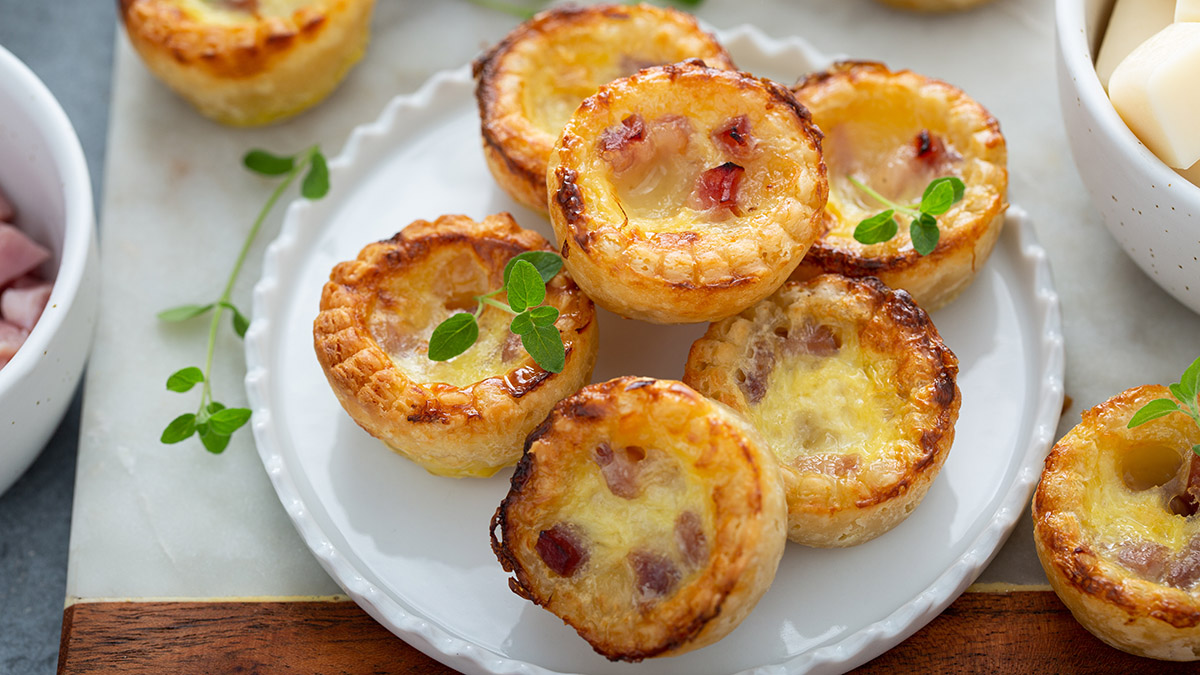 Image of mini carbonara quiches on a white plate on a wood board