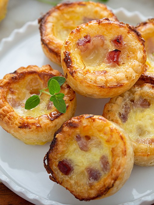 Image of mini carbonara quiches on a white plate on a wood board